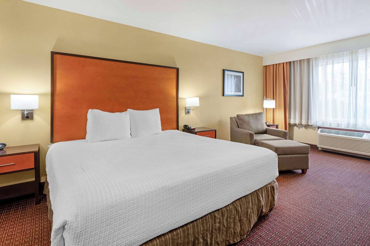 Une chambre d’hôtel avec un grand lit, une chaise, un bureau et une fenêtre avec des rideaux.
