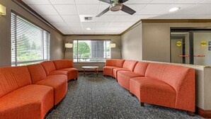 A hotel lobby with a seating area, a ceiling fan, and a view of the outdoors through the windows. - Best Western Cascade Inn & Suites (Wood Village)