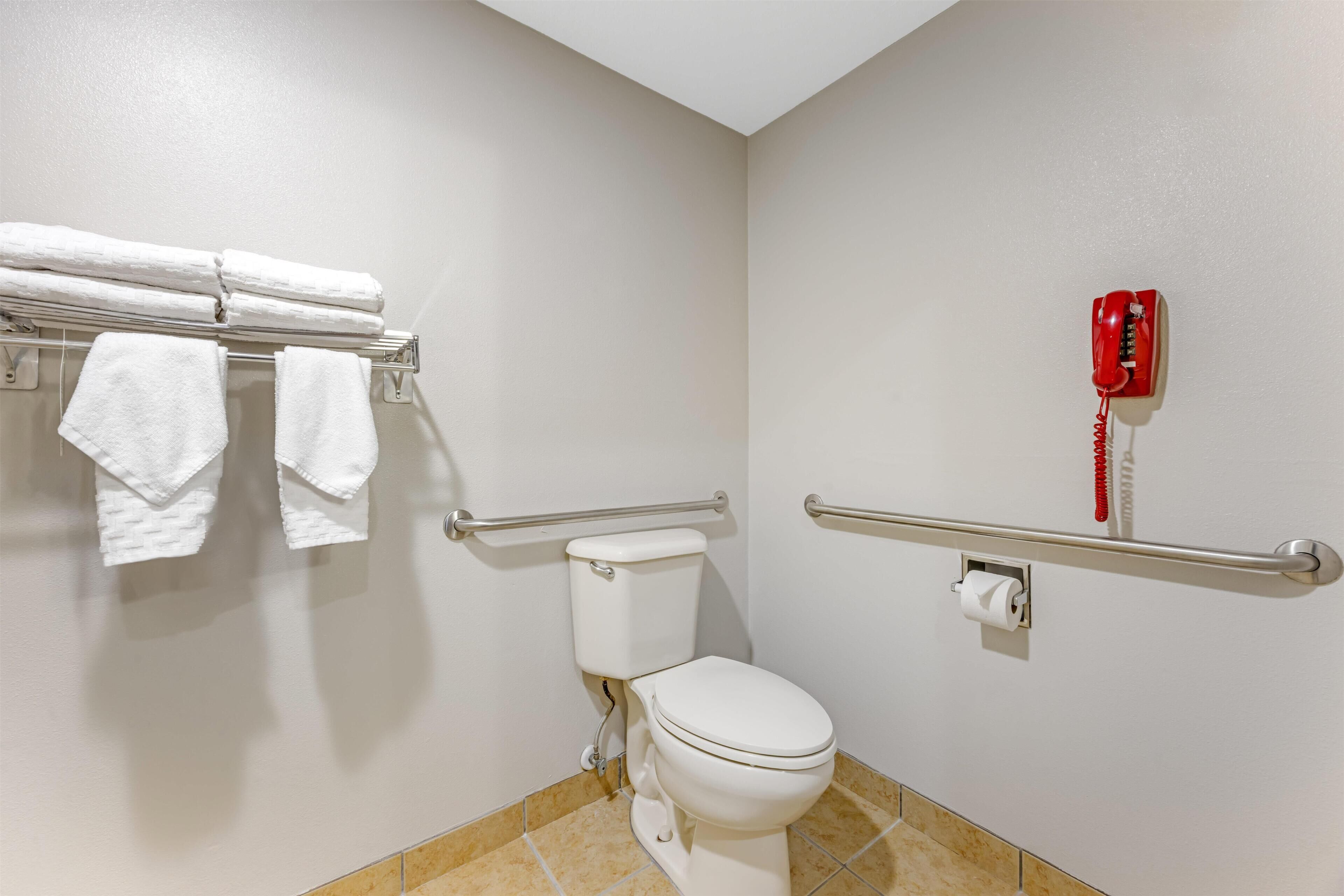 A bathroom with a toilet, a handrail, a towel rack with towels, and a red telephone.