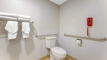 A bathroom with a toilet, a handrail, a towel rack with towels, and a red telephone.
