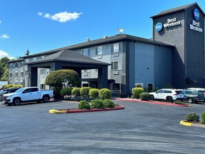 A Best Western hotel with a modern design, featuring a covered entrance and a parking lot with several vehicles.