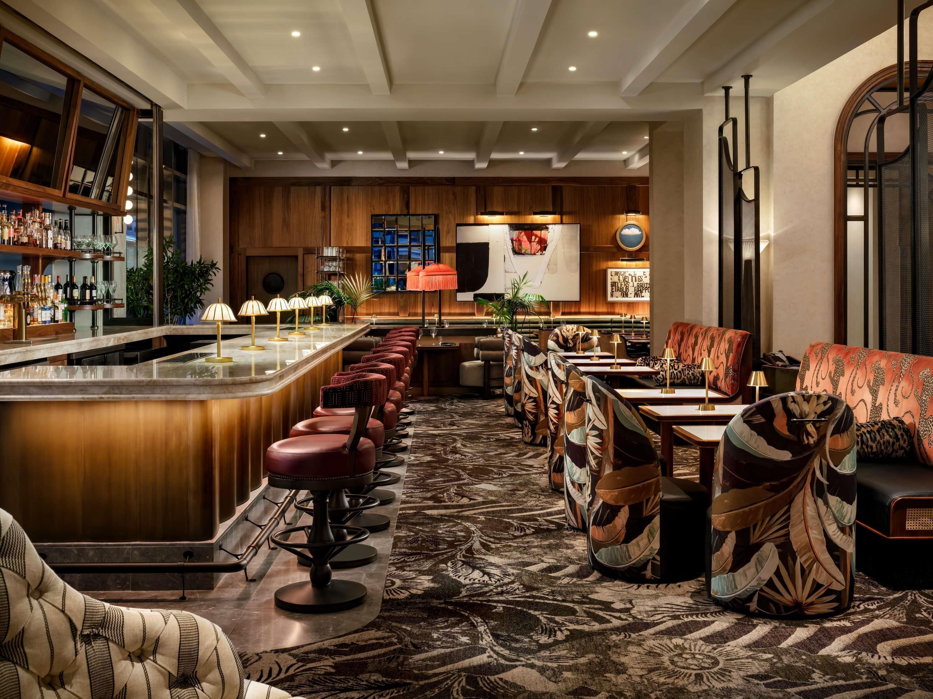 Een bar met een lange toonbank, meerdere krukken en een zithoek met gestoffeerde stoelen en banken.