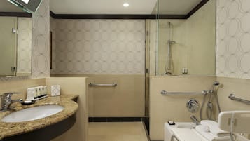 A modern bathroom with a granite sink, a glass shower enclosure, and a white vanity with a towel rack.