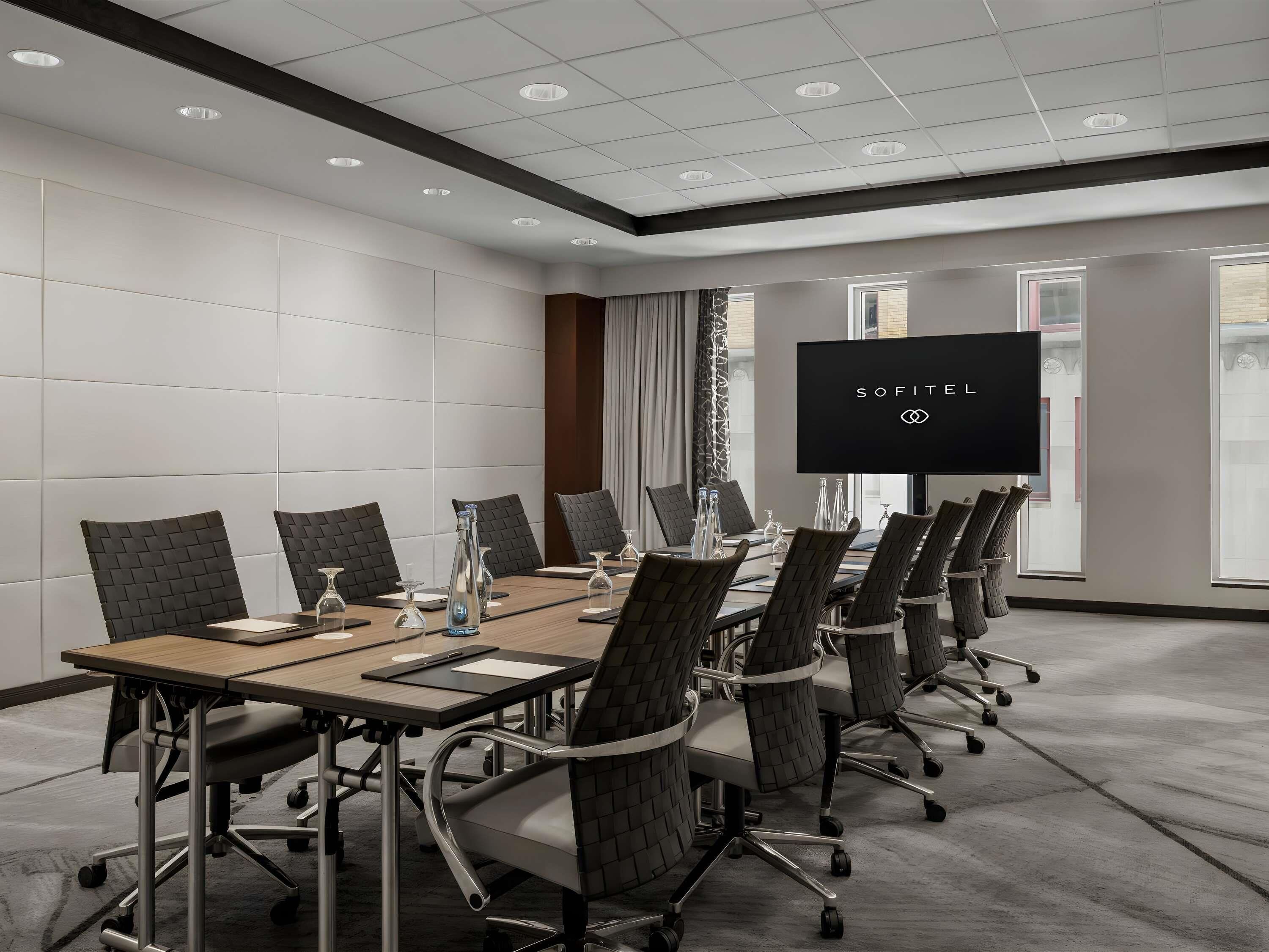 A conference room with a long table, chairs, a TV screen, and a window.