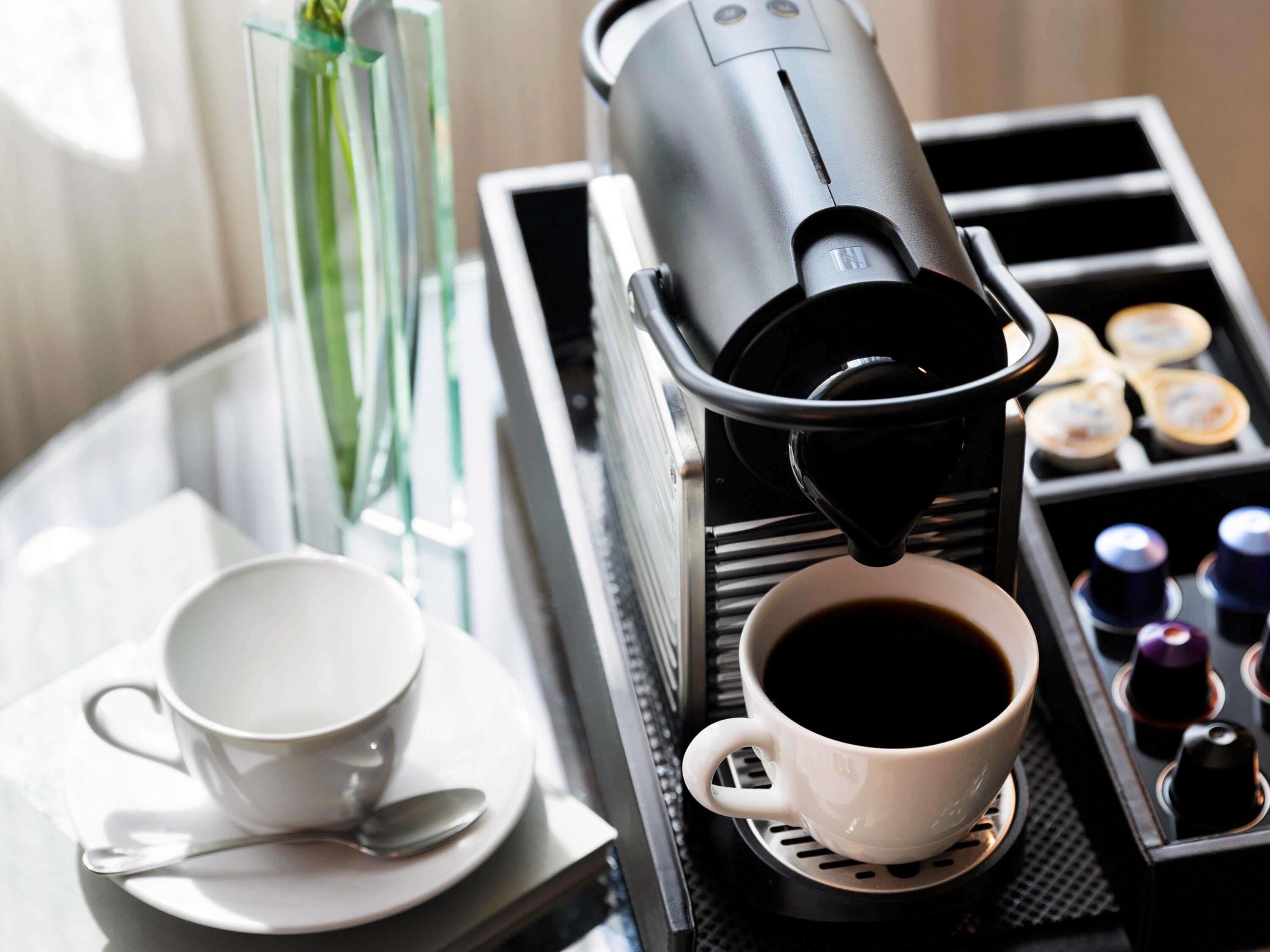 A coffee machine dispensing coffee into a cup, a tray with small containers, and a cup and saucer on a table.