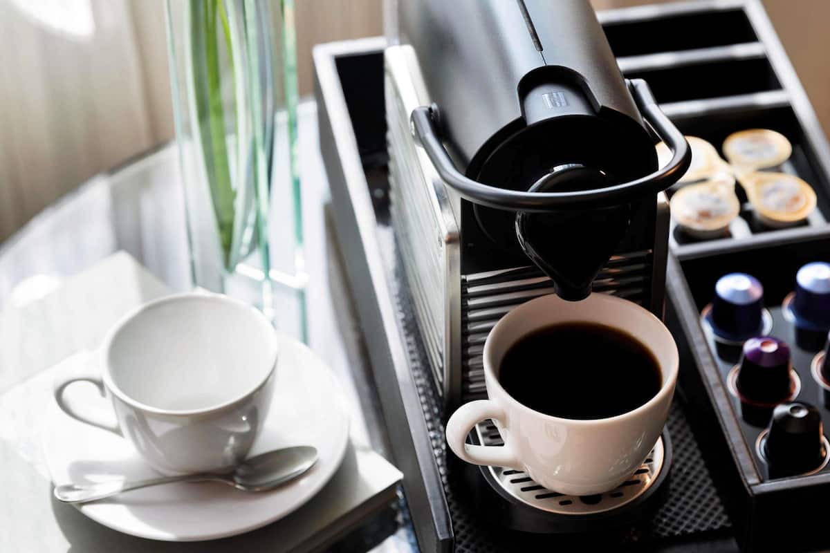 A coffee machine dispensing coffee into a cup, a tray with small containers, and a cup and saucer on a table.