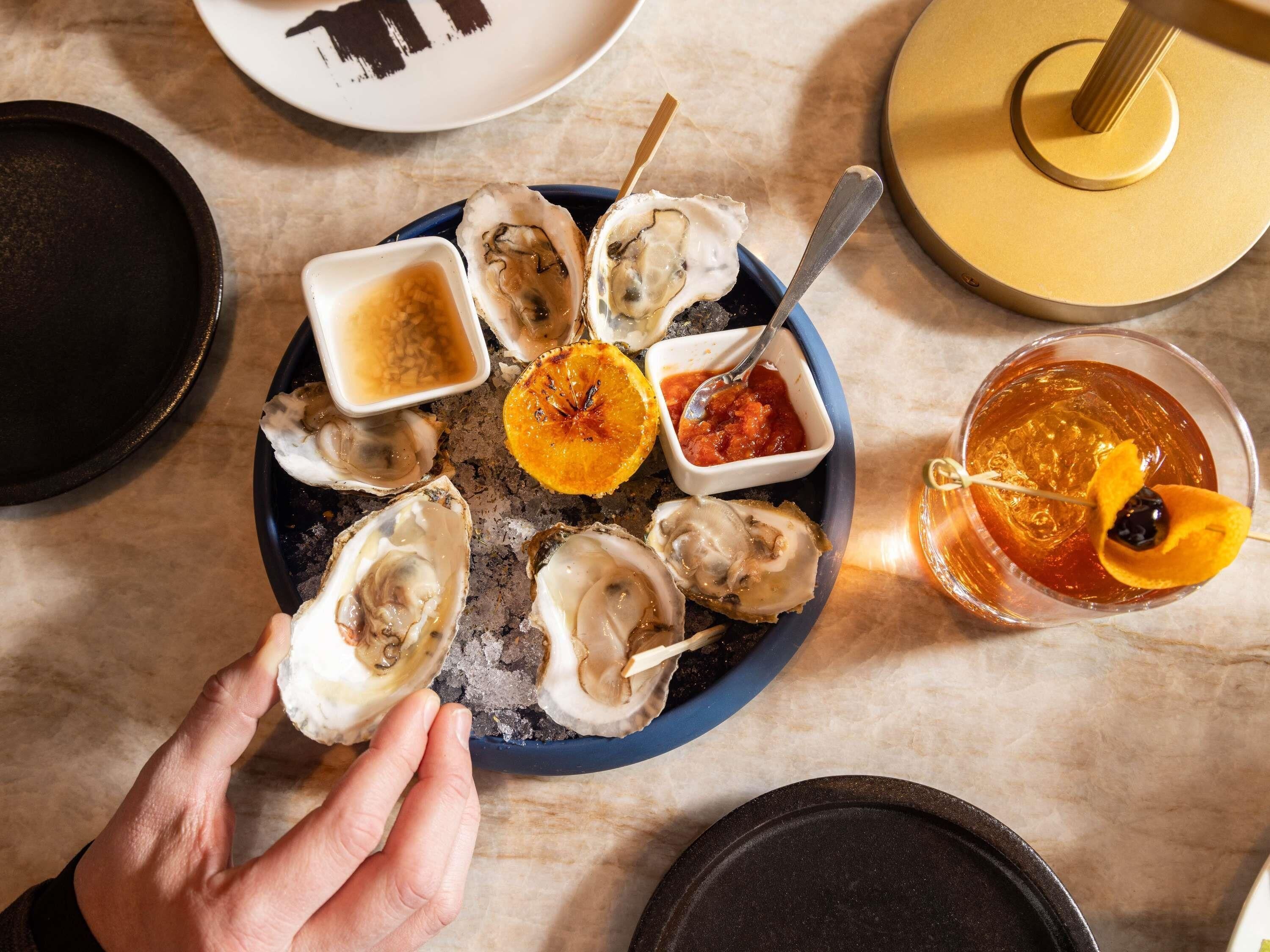 A plate of oysters with various condiments and a cocktail with an orange slice garnish.