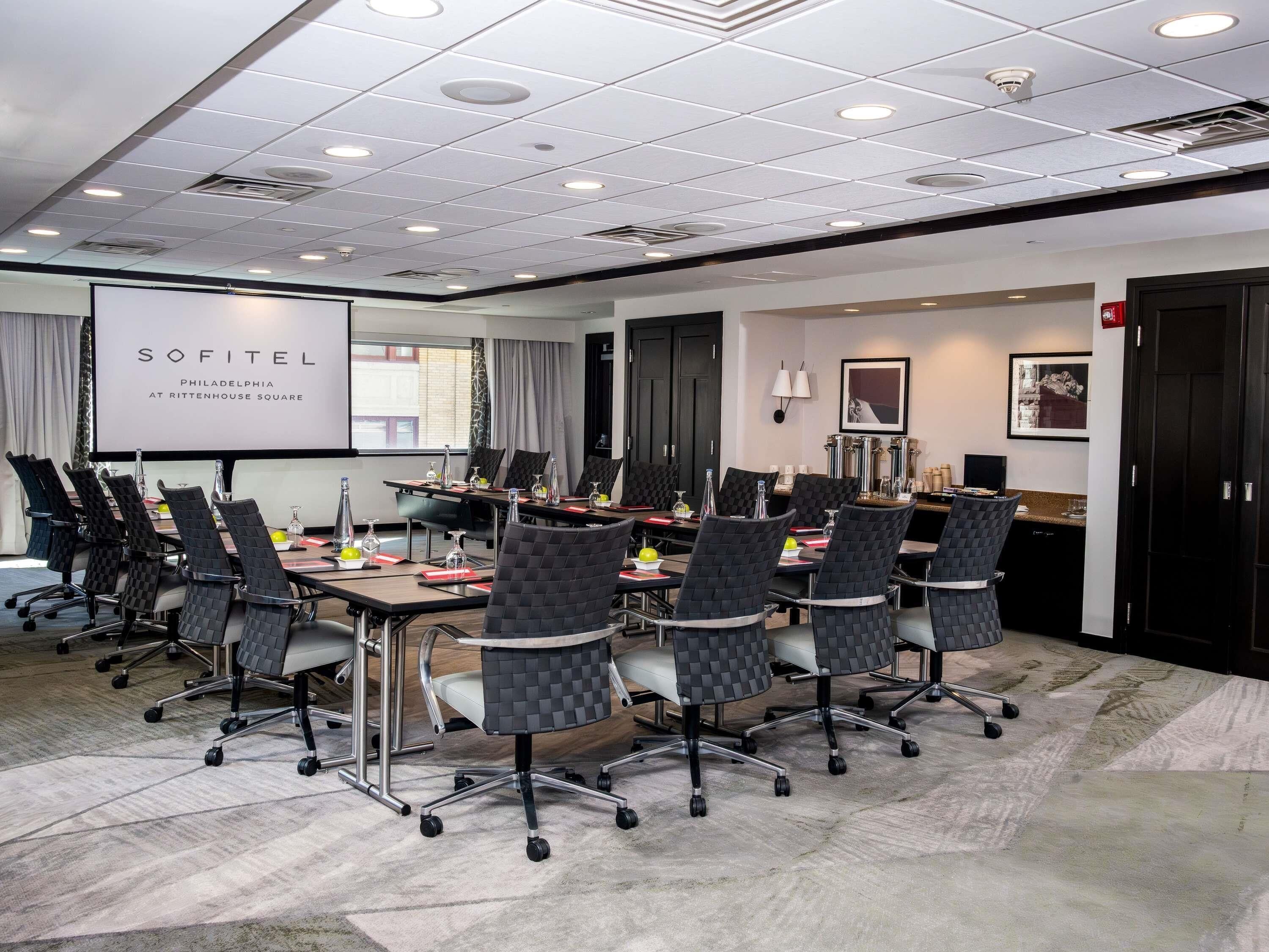 A conference room with a whiteboard, multiple chairs, a table with water bottles, and a projector screen.
