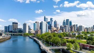 A city skyline with modern buildings, a river, and a pedestrian bridge.