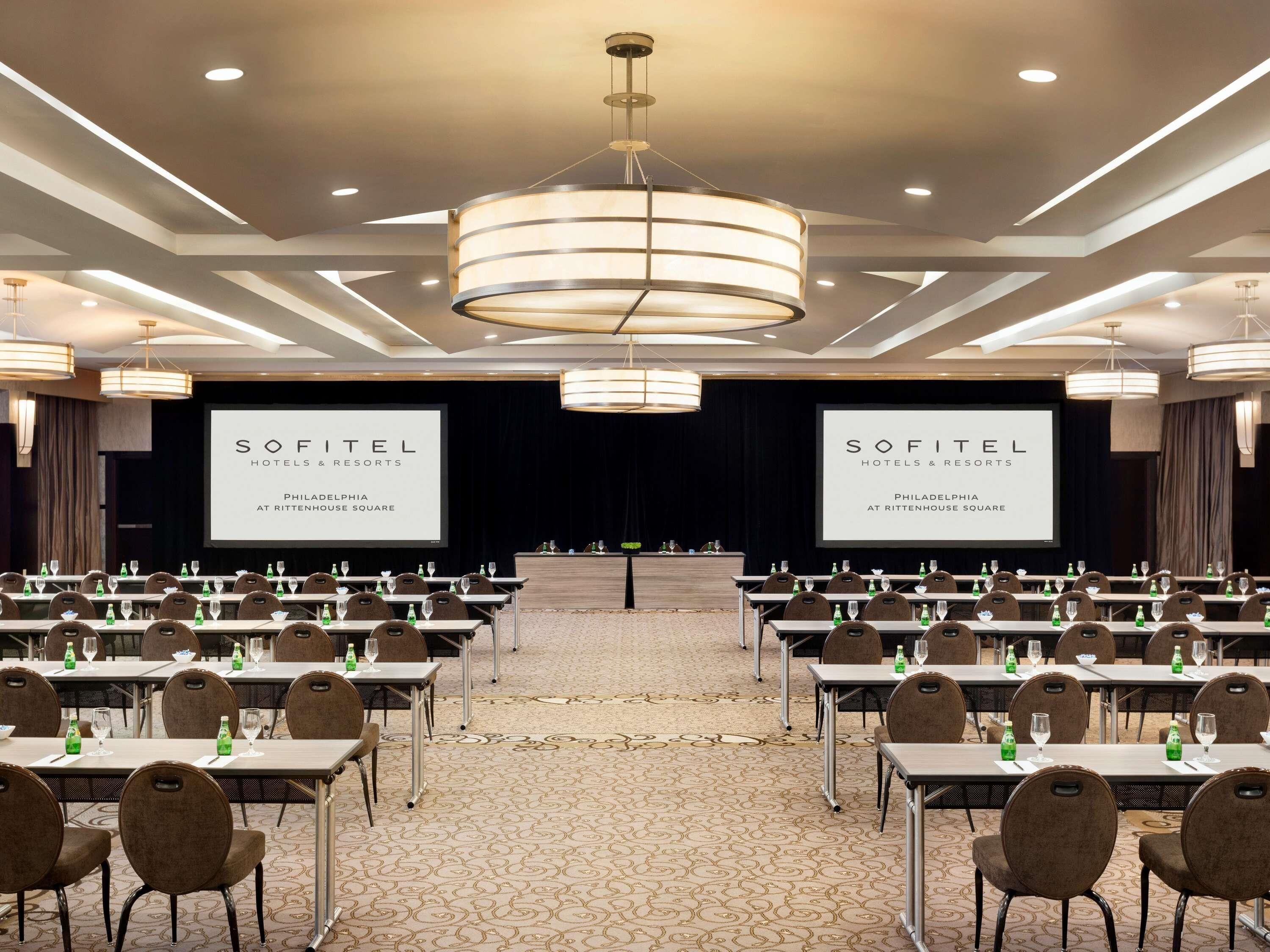 Un salón de conferencias con mesas, sillas y una gran pantalla mostrando 'SOFITEL HOTELS & RESORTS PHILADELPHIA AT RITTENHOUSE SQUARE'.
