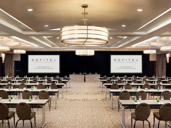 A conference room with tables, chairs, and a large screen displaying 'SOFITEL HOTELS & RESORTS PHILADELPHIA AT RITTENHOUSE SQUARE'.