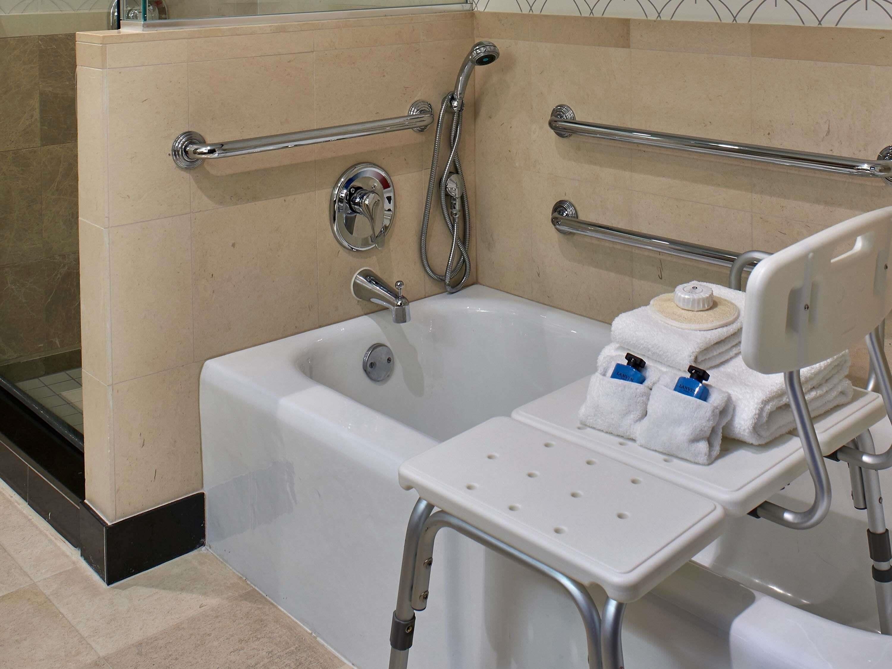 A bathroom with a bathtub, grab bars, a showerhead, and a towel rack.