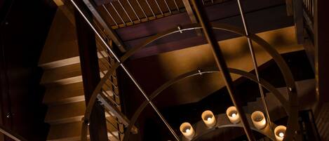A spiral staircase with a railing, a circular ceiling design, and multiple light fixtures.