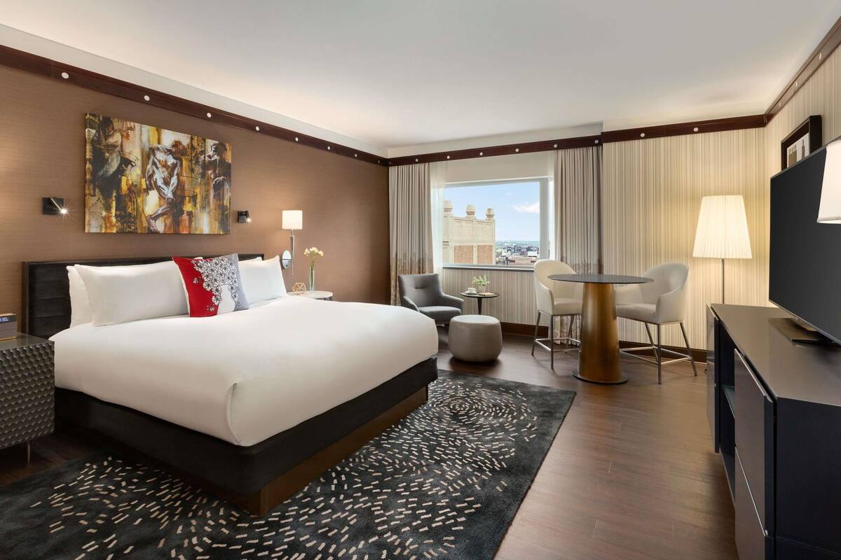 Habitación de hotel con una cama grande, un escritorio, una silla, un televisor y una ventana con vista a la ciudad.