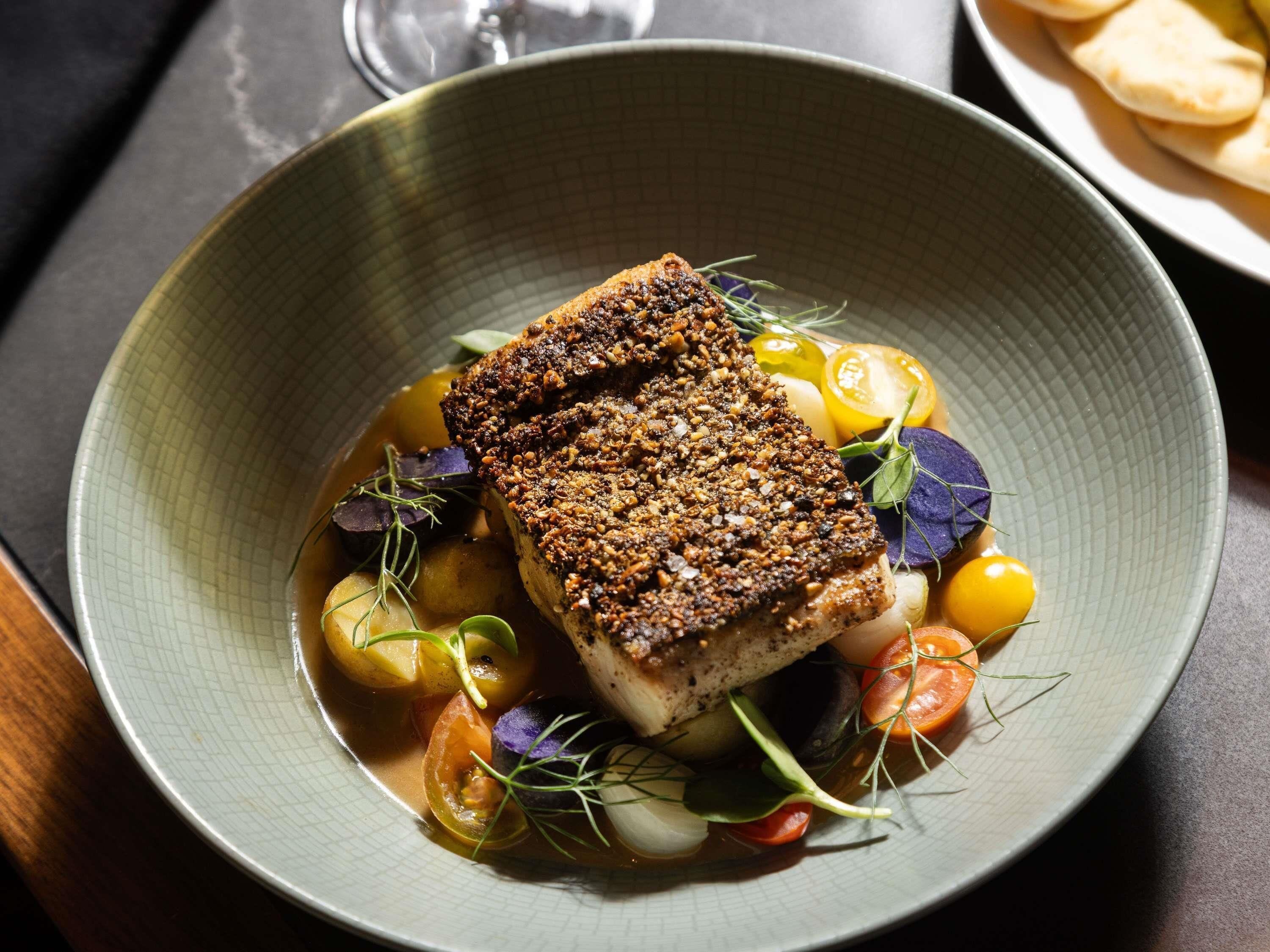 A dish with a crispy top, surrounded by vegetables and herbs.