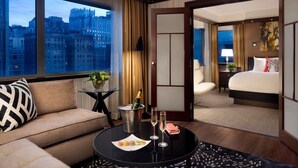 A hotel room with a sofa, a dining table with a bottle of champagne, and a view of the cityscape. - Sofitel Philadelphia at Rittenhouse Square (Philadelphia)