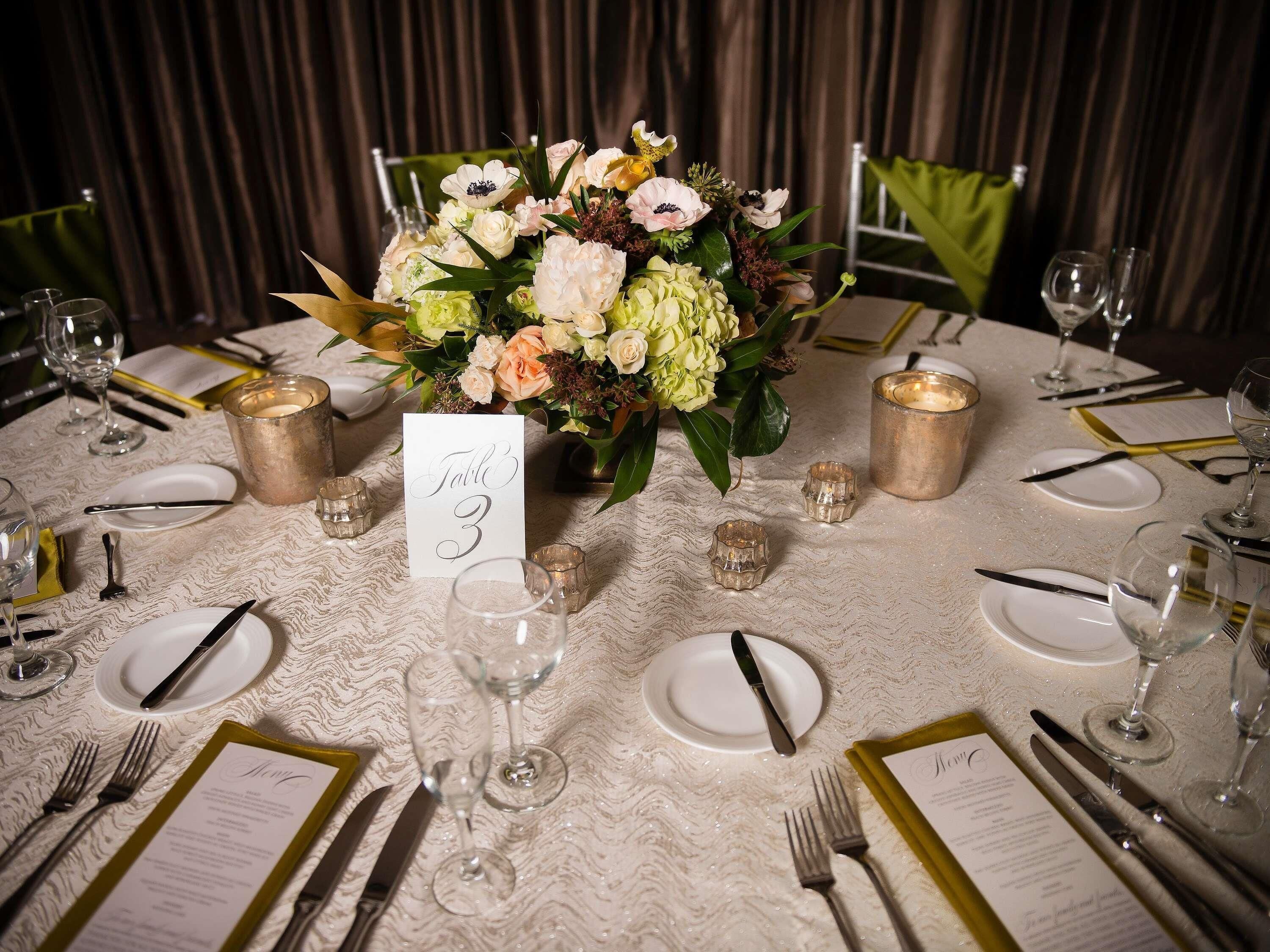 A table set for a formal event with a floral centerpiece, numbered placemats, and candle holders.