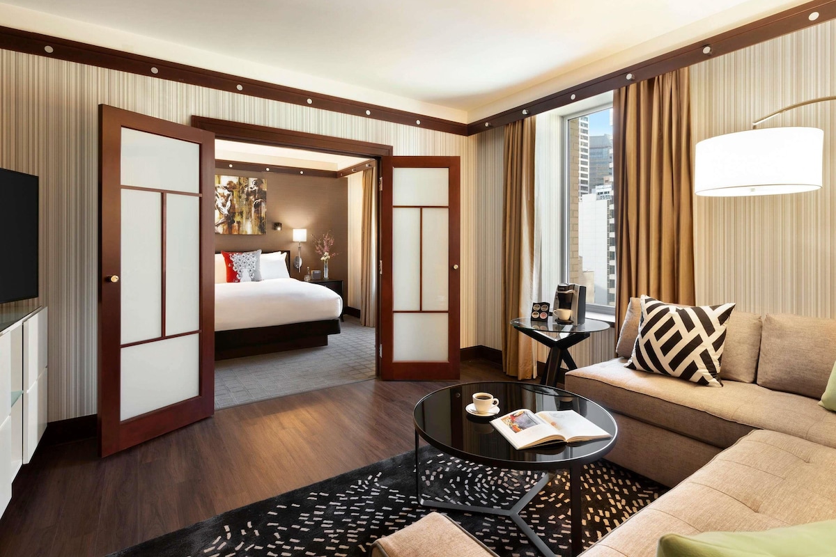 A hotel room with a bed, a sofa, a coffee table, and a TV.