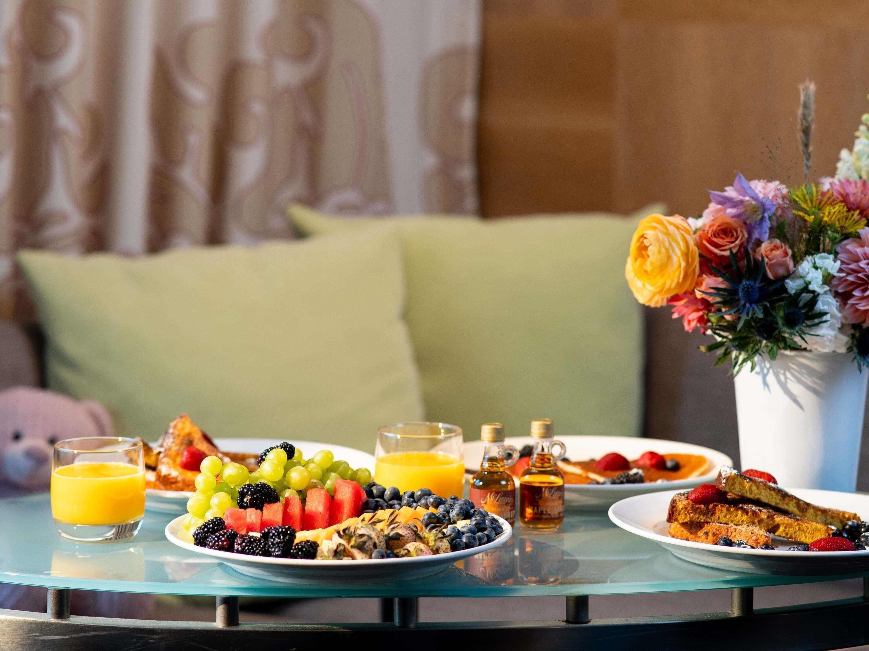 A breakfast table with plates of food, glasses of orange juice, and a vase of flowers.