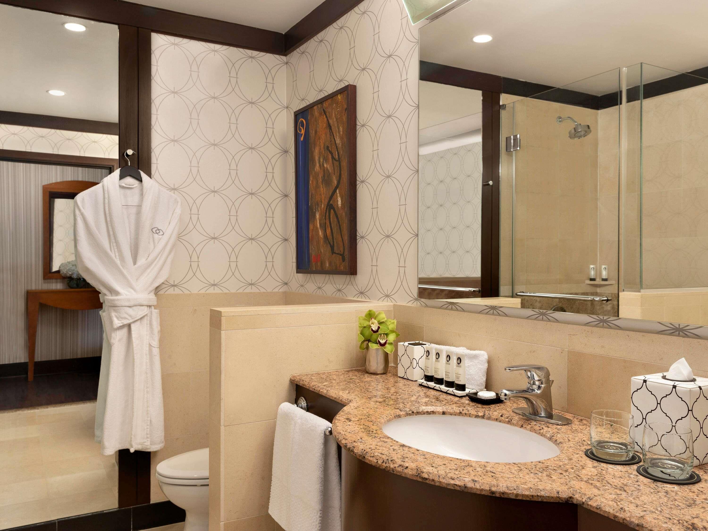 A modern bathroom with a granite countertop, a white sink, and a glass shower enclosure.