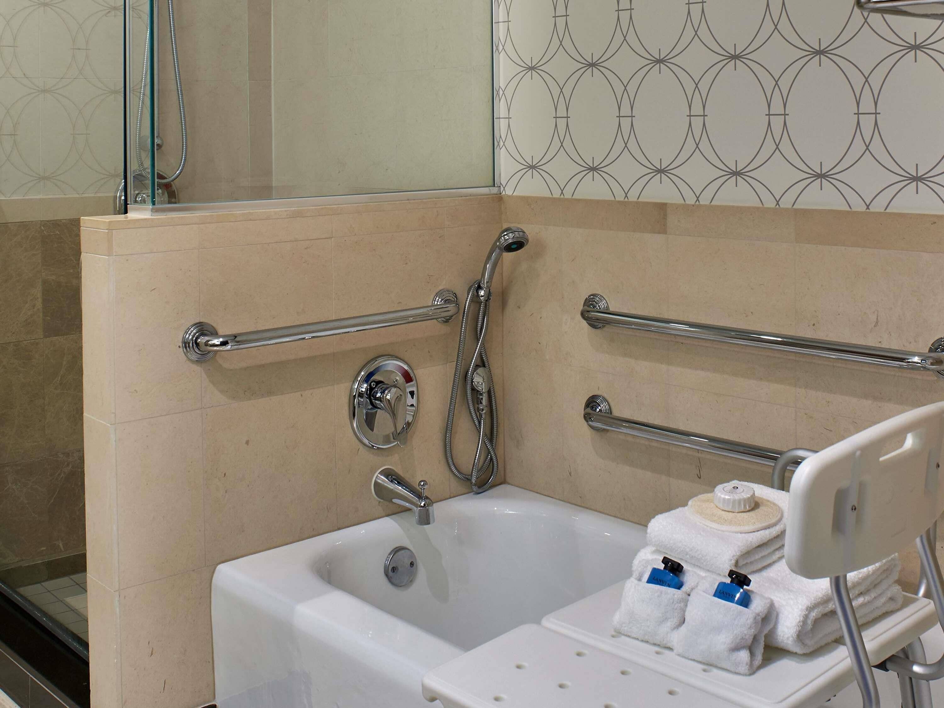 Un baño con bañera, barras de apoyo, cabezal de ducha y toallero.