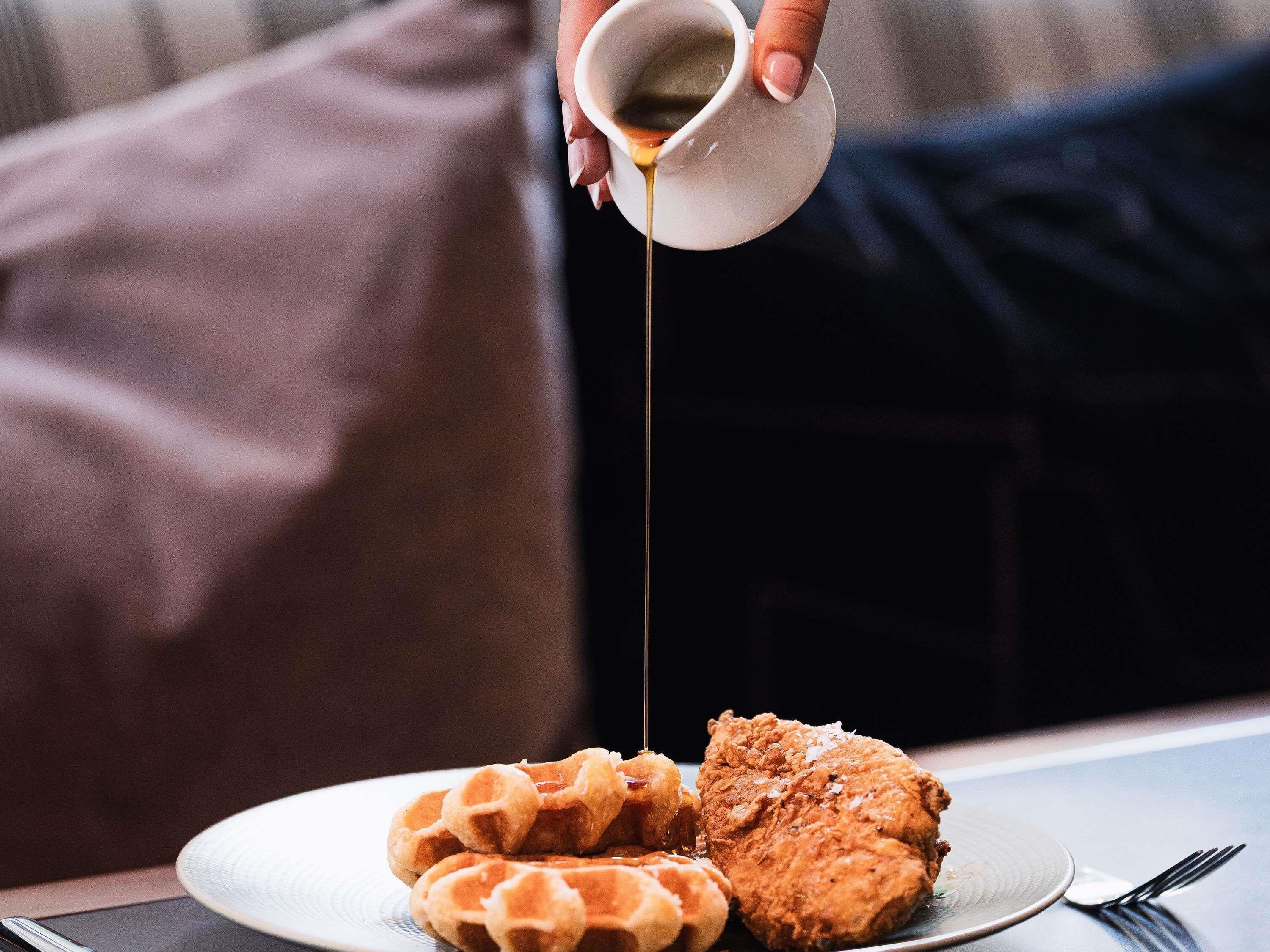 Une assiette avec des gaufres et du poulet frit, le tout nappé de sirop.