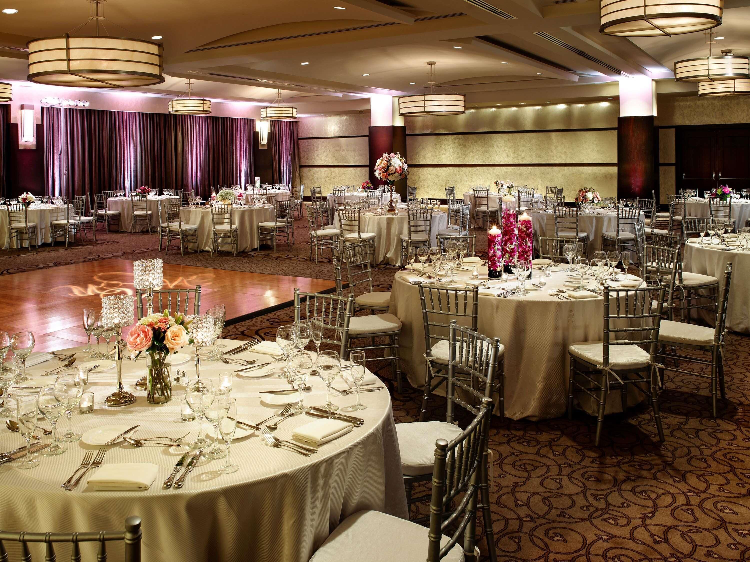 A banquet hall with round tables, chairs, and floral centerpieces.