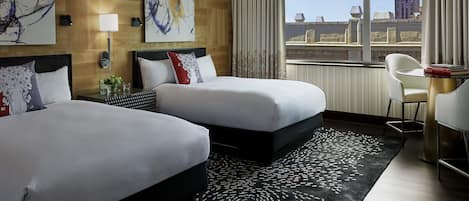 A hotel room with two beds, a large abstract painting on the wall, a view of the city through the window, and a modern desk with a chair.
