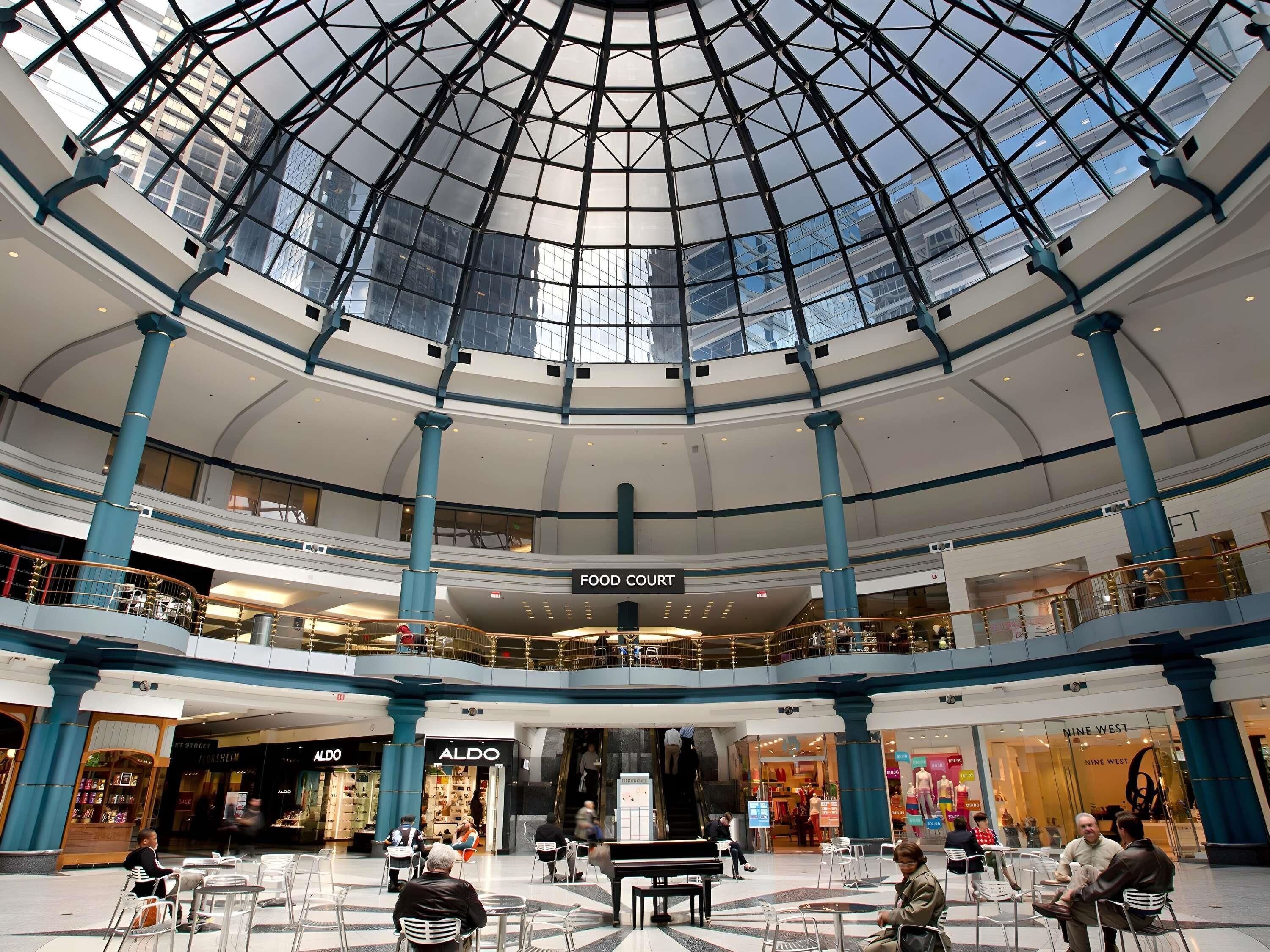 Un centro comercial de varios niveles con techo de vidrio, múltiples plantas y diversas tiendas, incluyendo un patio de comidas.