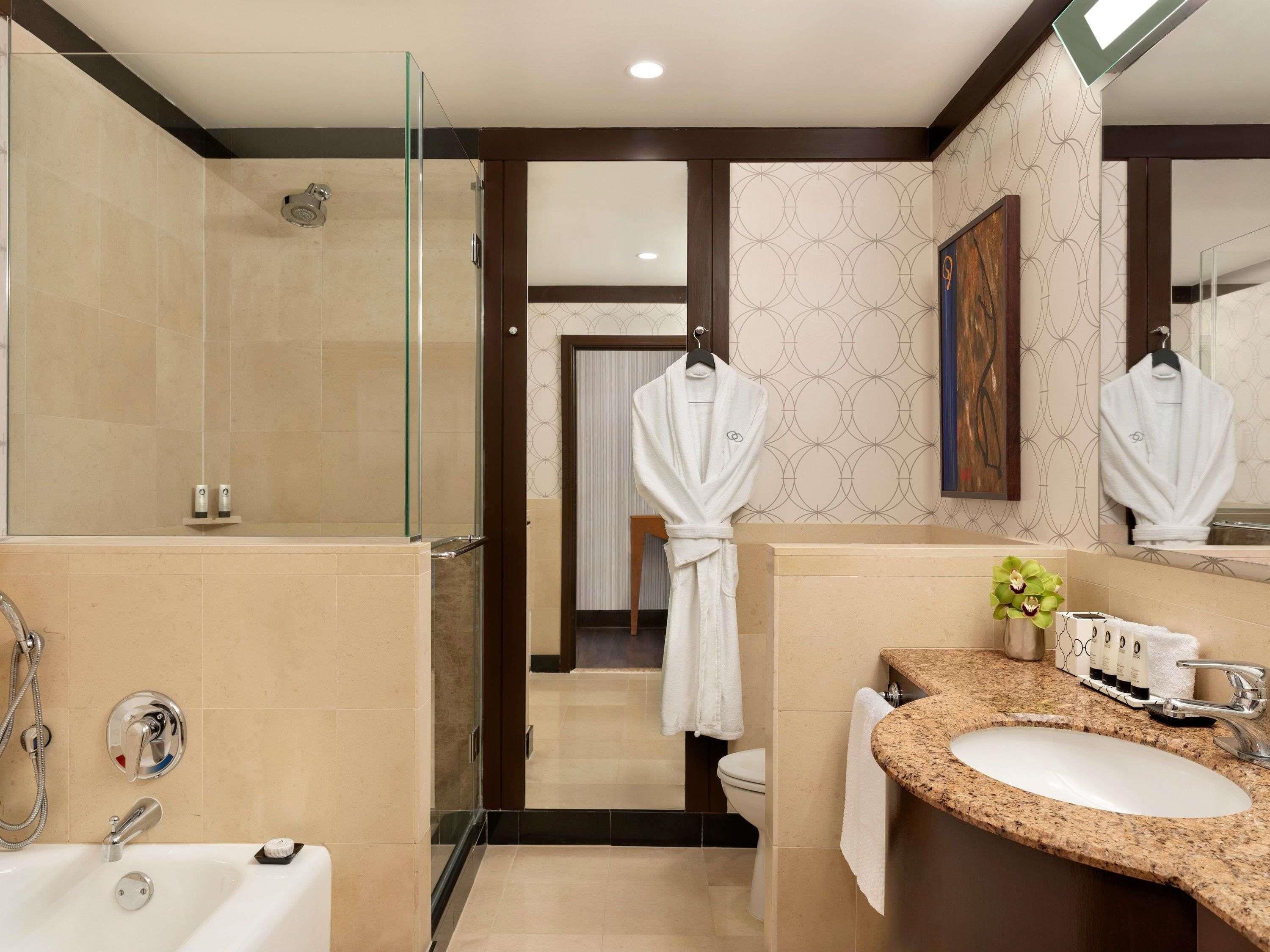 Une salle de bain moderne dotée d’une douche à parois de verre, d’une baignoire sur pieds, d’un lavabo encastré dans un plan de travail en granit et d’un grand miroir.