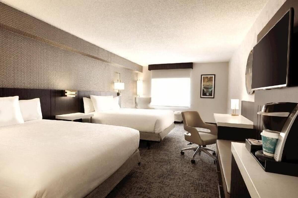 Quarto de hotel com duas camas, uma mesa, uma cadeira, televisão de tela plana e máquina de café.