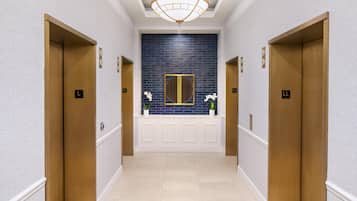 Corredor com dois elevadores, parede revestida de azulejos azuis e painel branco com desenho circular.