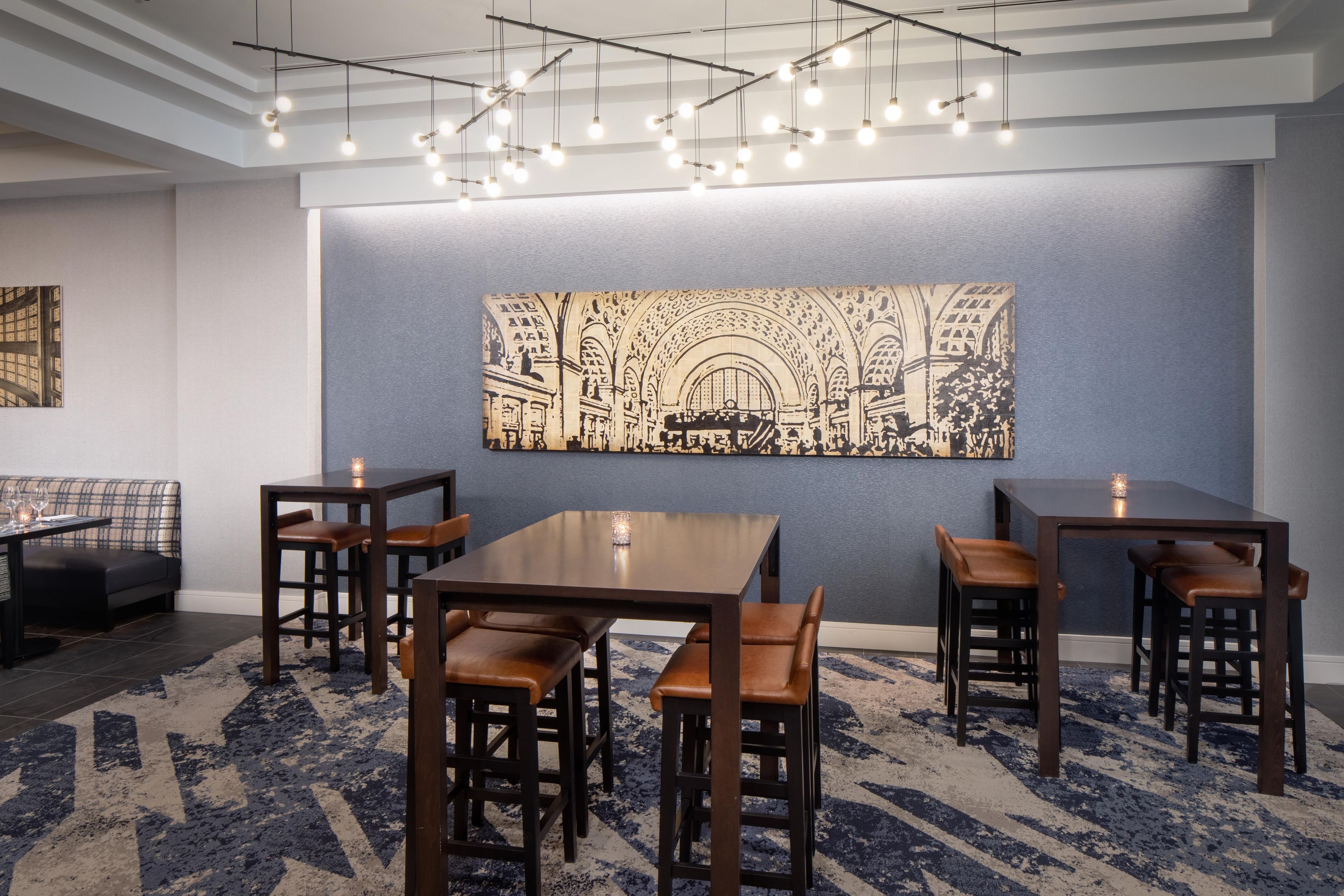 A modern dining area with a high ceiling, pendant lighting, and a large abstract artwork on the wall.