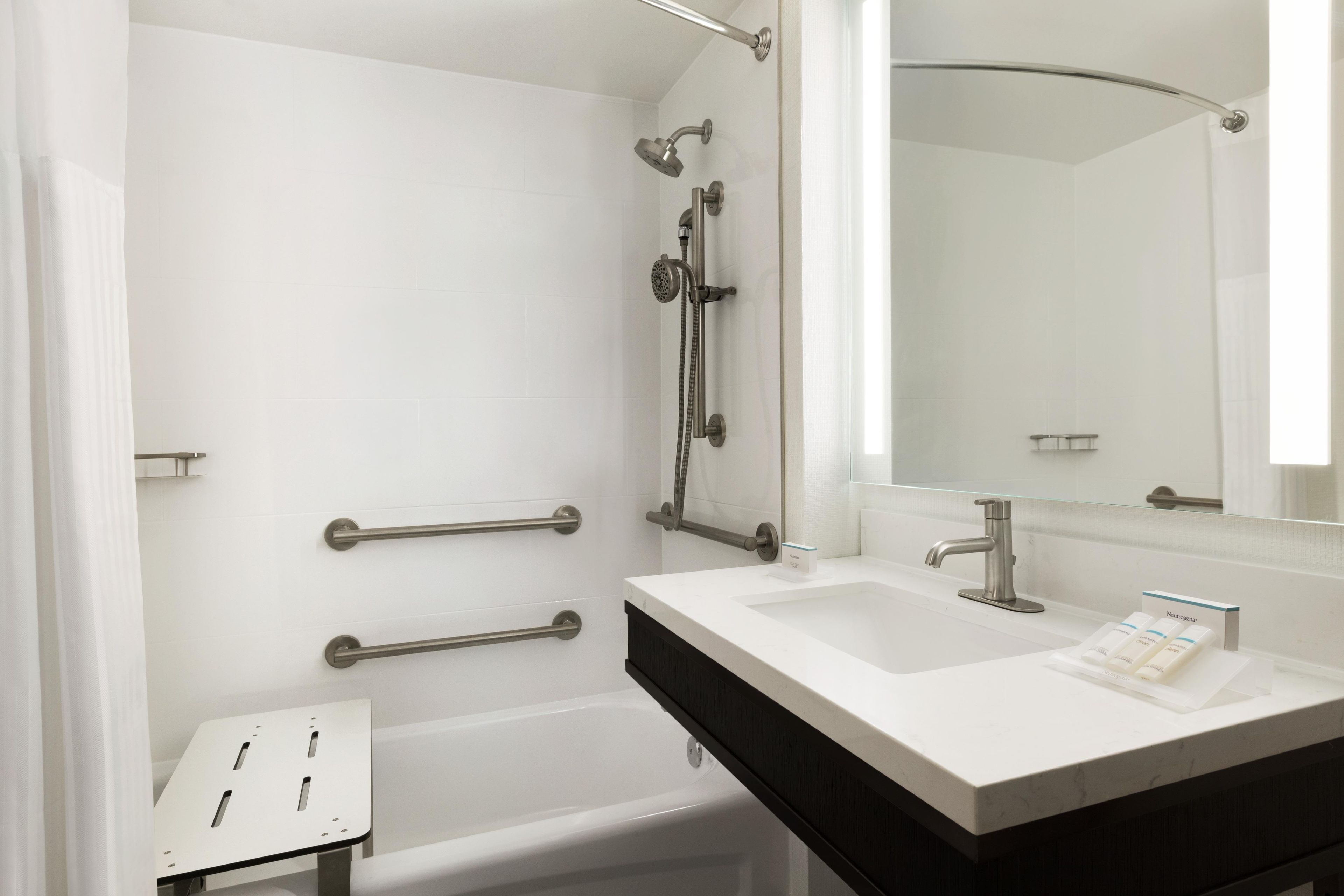 A modern bathroom with a bathtub, a shower, a vanity with a mirror, and handrails.