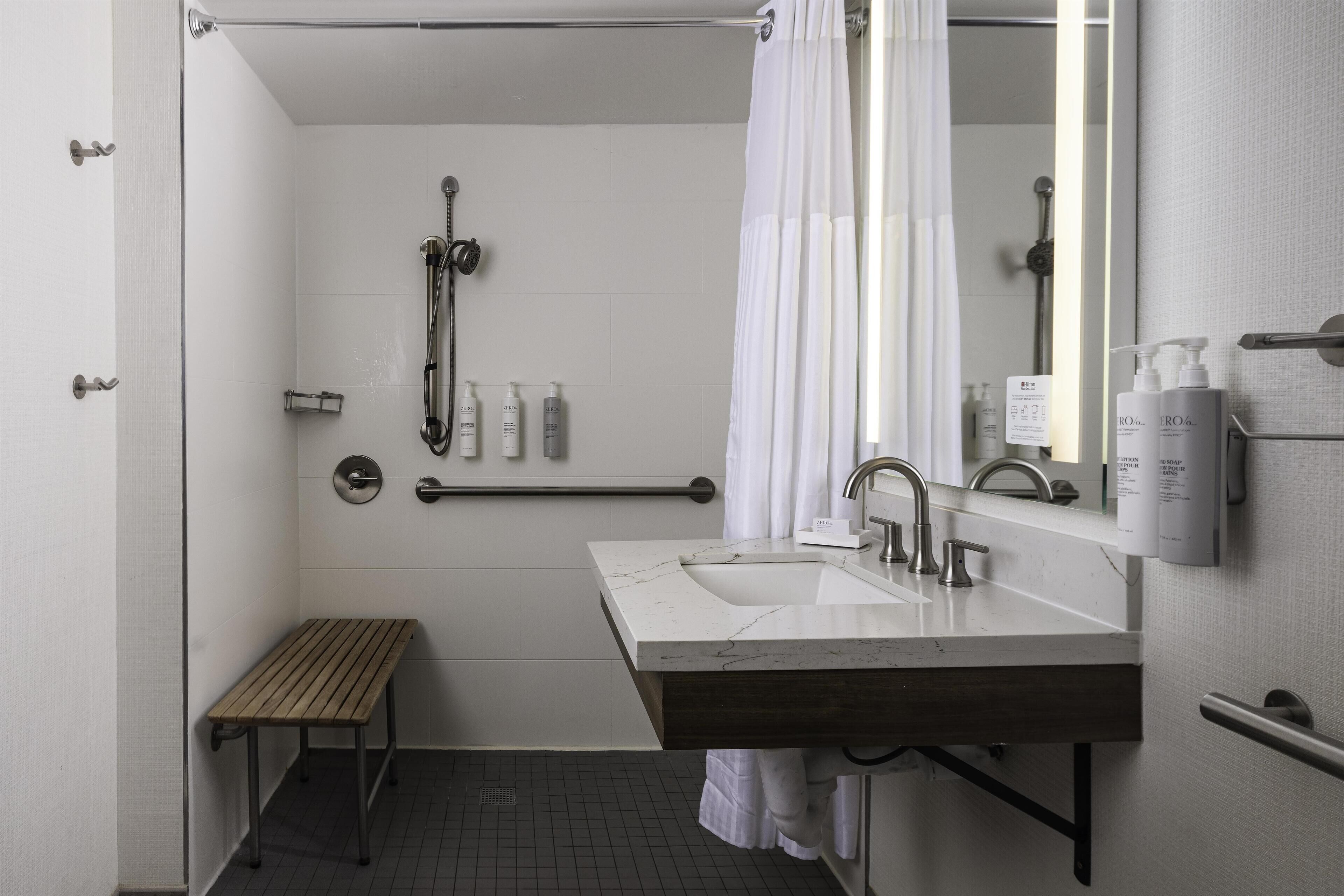 Une salle de bain moderne avec un lavabo blanc, un miroir, une douche et un banc.