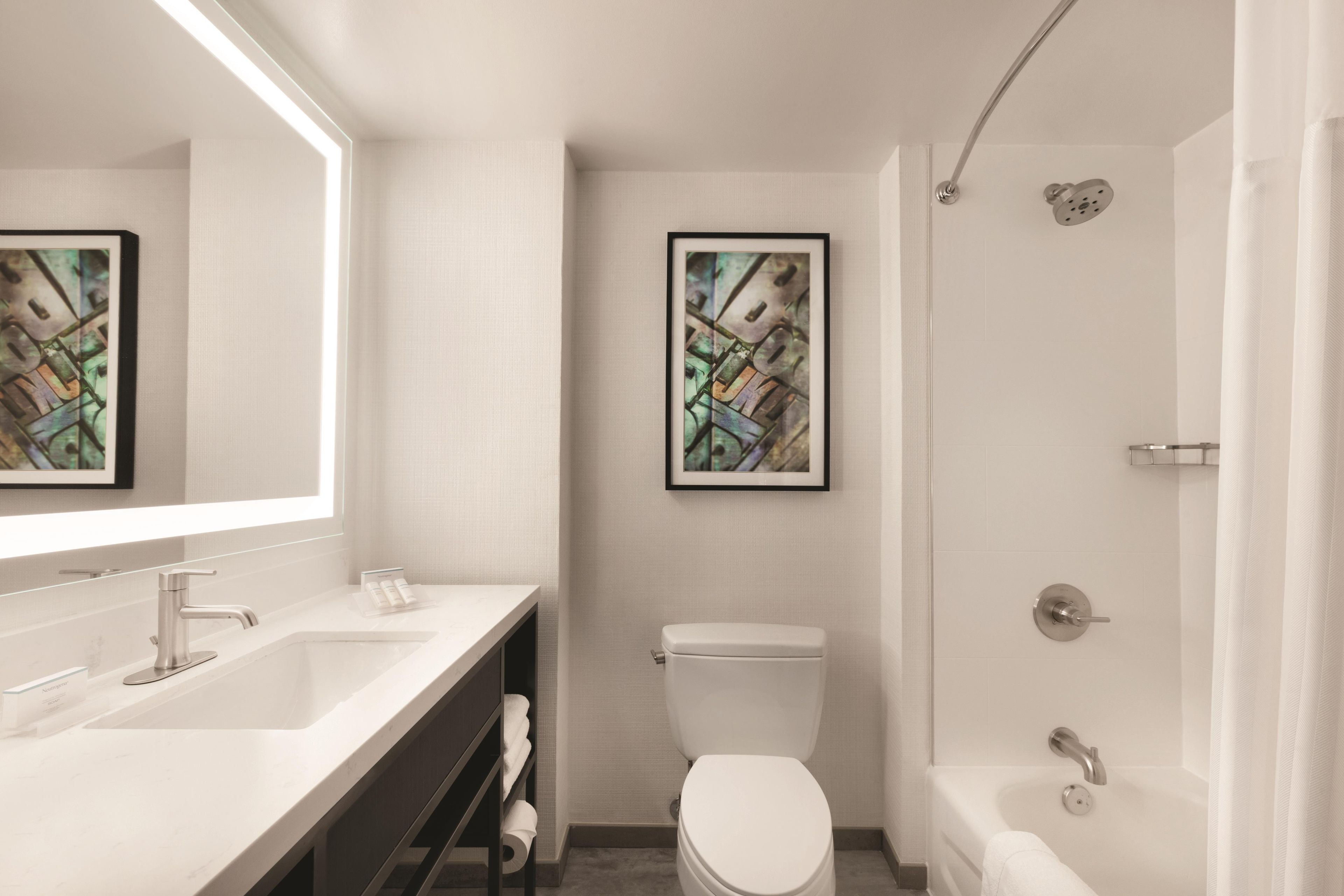 A modern bathroom with a white sink, toilet, and bathtub. There are two framed artworks on the walls.