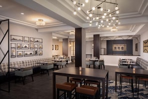 Un espace de restauration moderne offrant de nombreuses options de sièges, notamment des tables et des banquettes, ainsi qu’une variété de luminaires fixés au mur.
