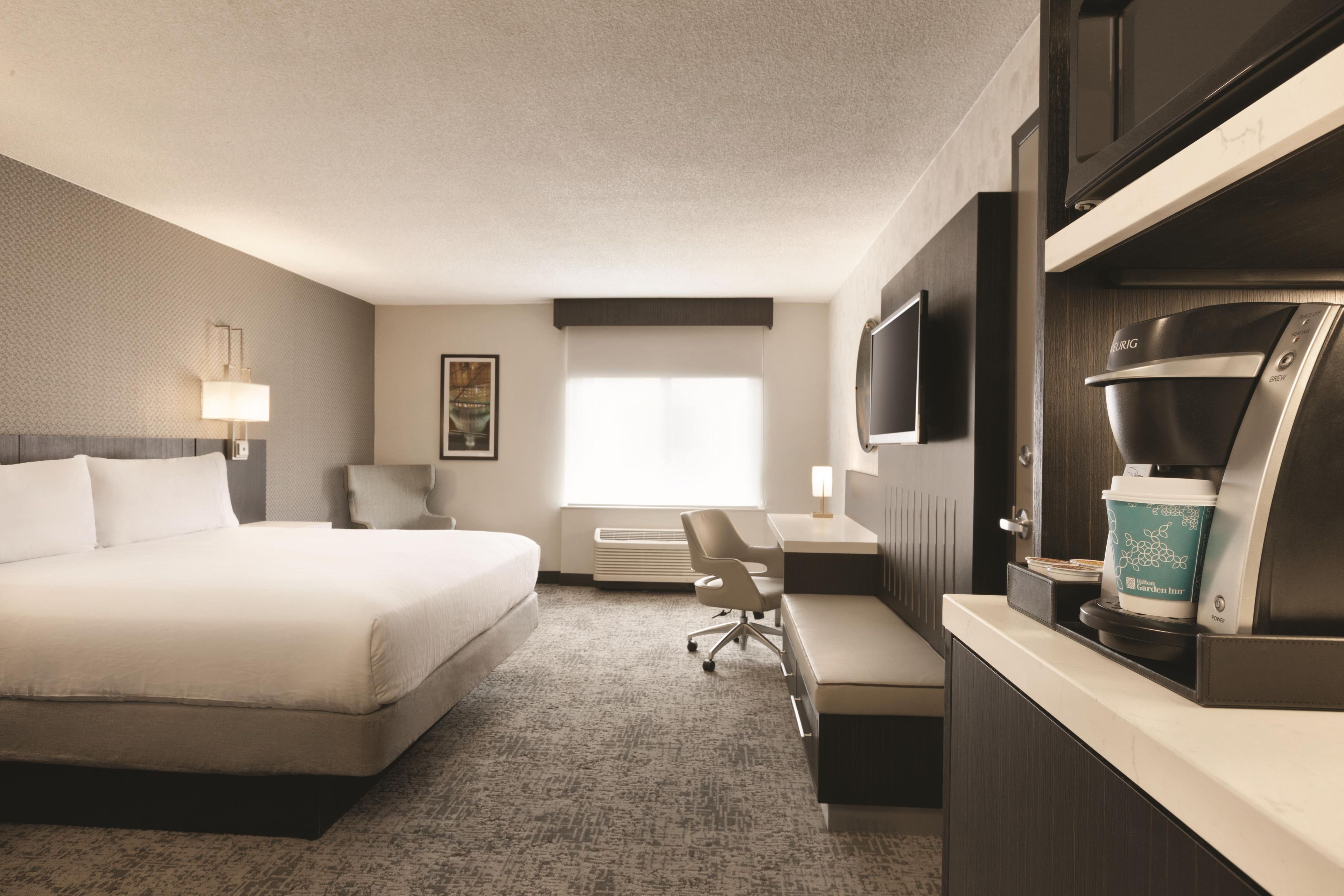 A hotel room with a bed, desk, chair, television, and a coffee machine.