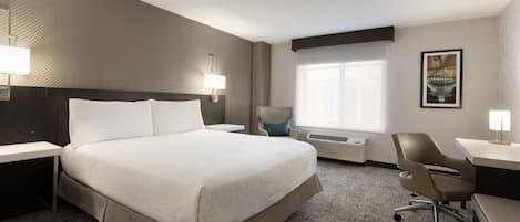A hotel room with a large bed, bedside tables, a desk, a chair, a window with a view, and a wall-mounted picture.