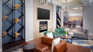Un salon moderne avec un canapé en cuir marron, un fauteuil vert, un téléviseur à écran plat, une cheminée et un coin repas agrémenté d’un mur à motifs et de luminaires suspendus.