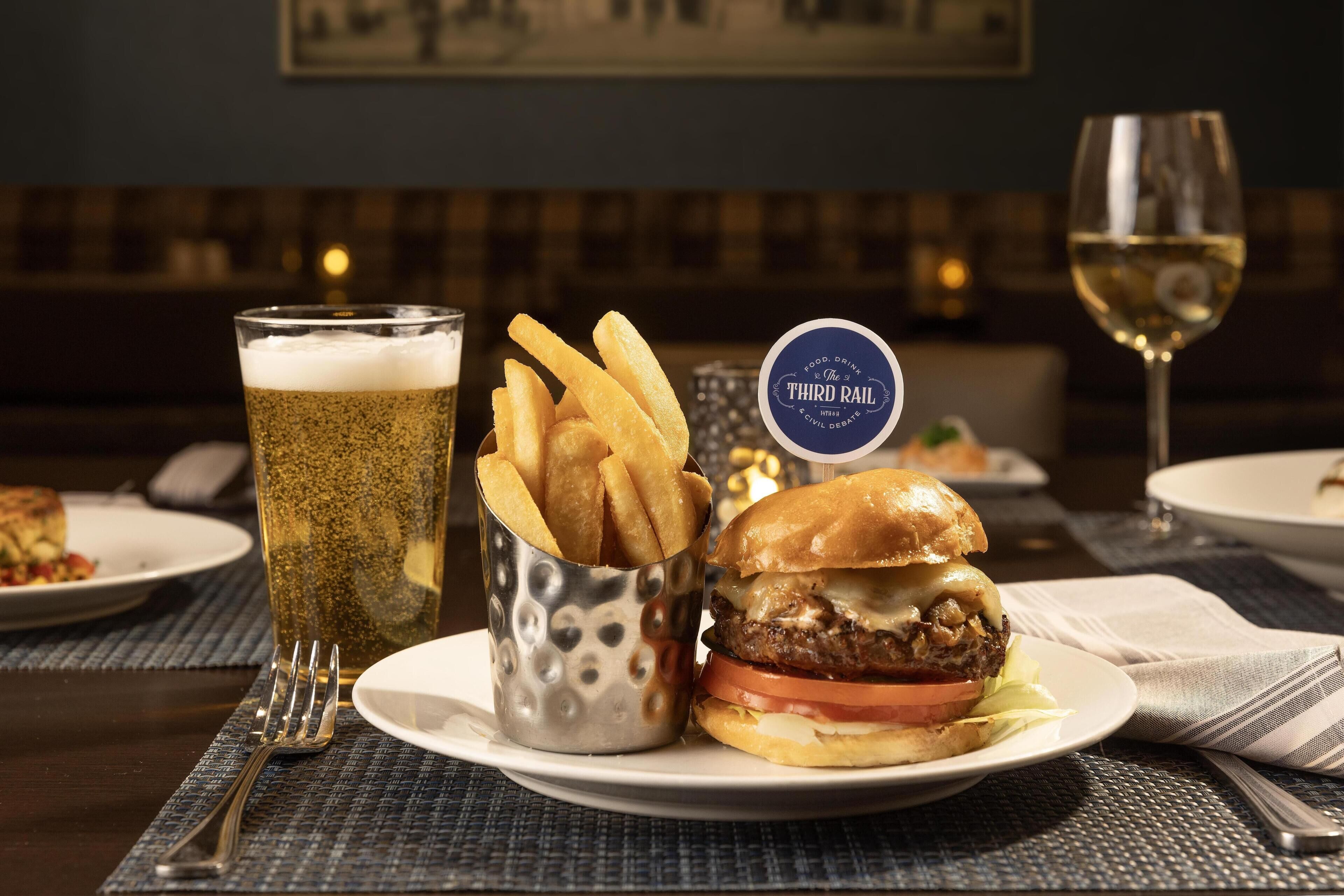 A meal with a burger, fries, and a beer glass on a table with a placemat.
