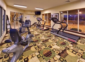 A fitness center with cardio machines, a mirrored wall, and a patterned carpet.