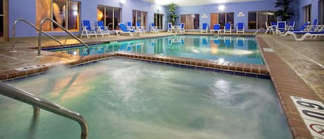 An indoor swimming pool with multiple lanes, lounge chairs, and a clear water surface.