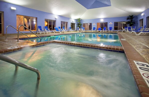 An indoor swimming pool with multiple lanes, lounge chairs, and a clear water surface.