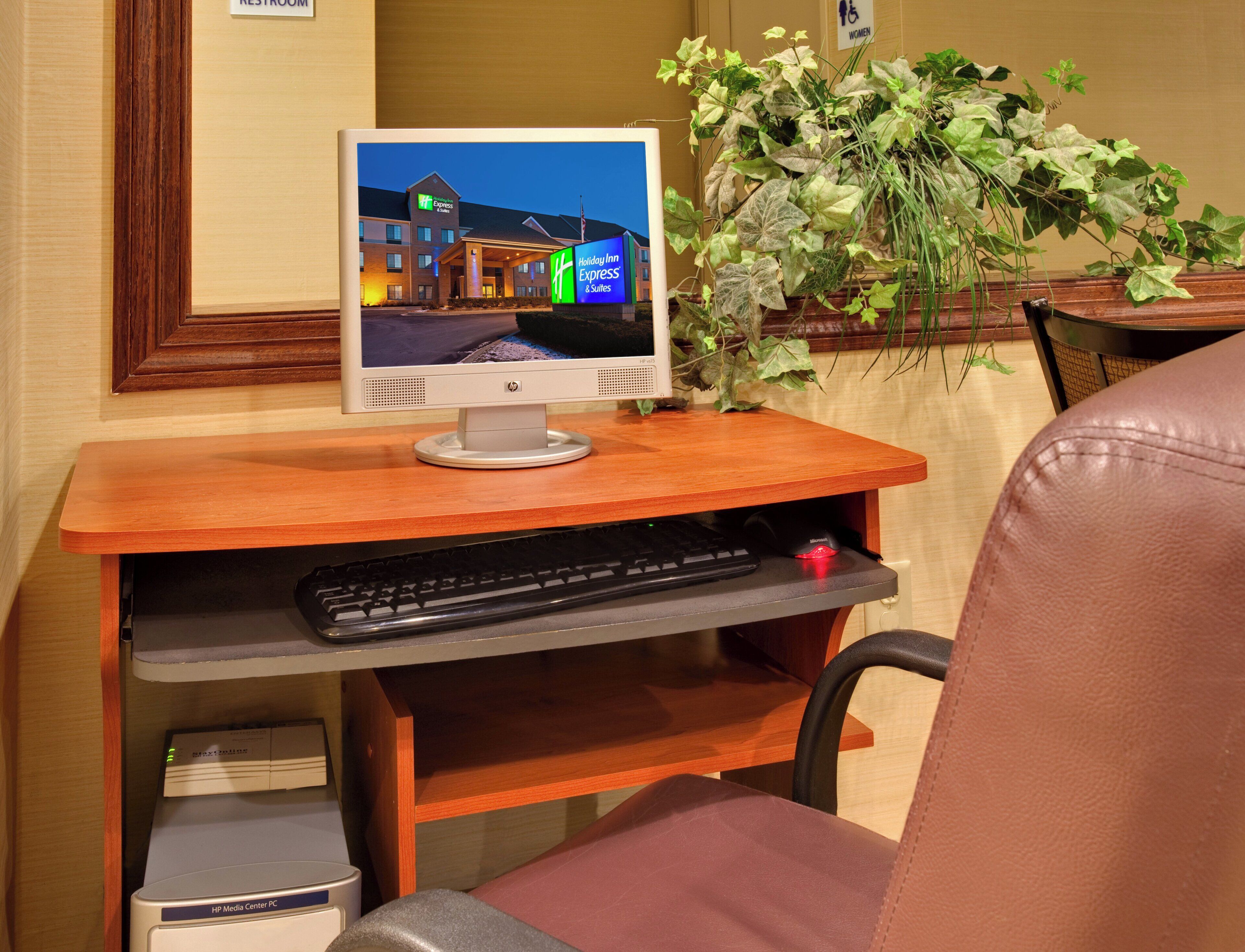 A computer monitor on a wooden desk with a keyboard and a trash bin underneath.