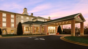 A hotel with a covered entrance, brick facade, and a parking lot. - Hilton Garden Inn Williamsburg (Williamsburg)