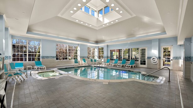 A large indoor swimming pool with multiple lanes, surrounded by lounge chairs and a sunroof ceiling. - Hilton Garden Inn Williamsburg (Williamsburg)