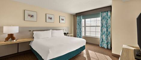 A hotel room with a large bed, a desk with a lamp, a TV, and a window with curtains.
