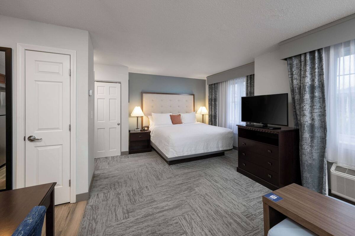 A hotel room with a bed, two bedside tables with lamps, a TV, a desk, and a chair.