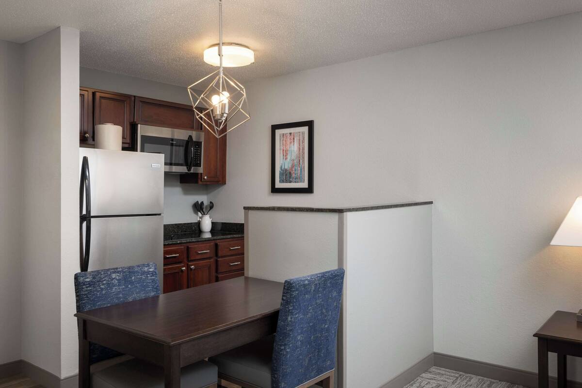 A compact kitchen with a refrigerator, microwave, and stove, a dining table with chairs, and a pendant light.